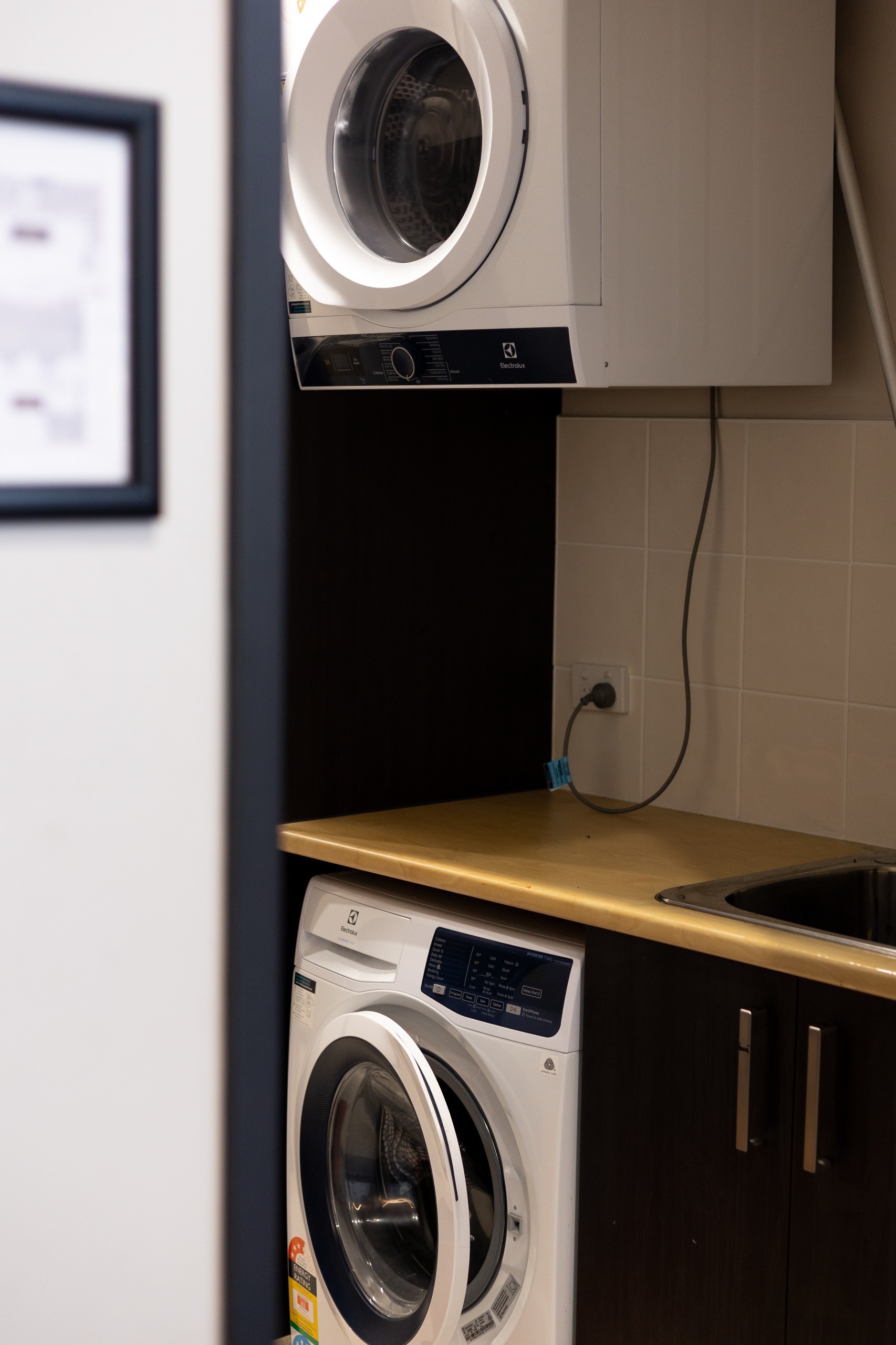Laundry room including a washing machine under the bench and sink with the dryer installed above.