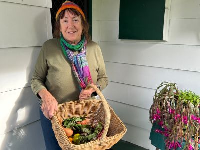 Jessica holding a basket of fresh vegetables out the front of her home.